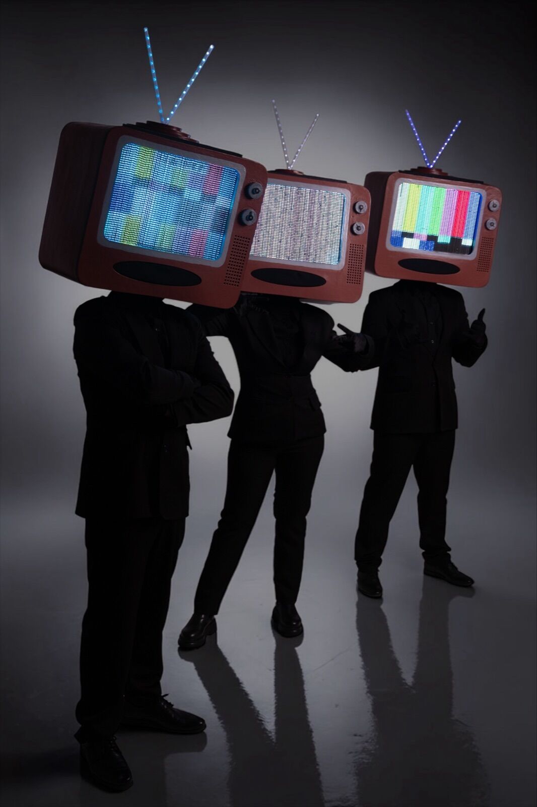 Three performers in black suits with retro TV heads, each screen showing a different test pattern